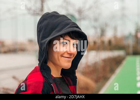 Ritratto di giovane donna che indossa il cappuccio sorridendo alla macchina fotografica Foto Stock