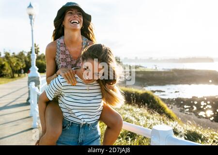 Carefree giovane donna suora piggybacking sul sentiero durante la giornata di sole Foto Stock