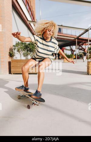 Donna bionda con braccia allungate skateboard sul sentiero durante il sole giorno Foto Stock