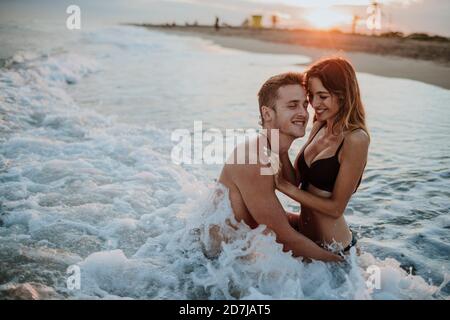 Una coppia sorridente si diverta mentre si siede in acqua sulla spiaggia Foto Stock