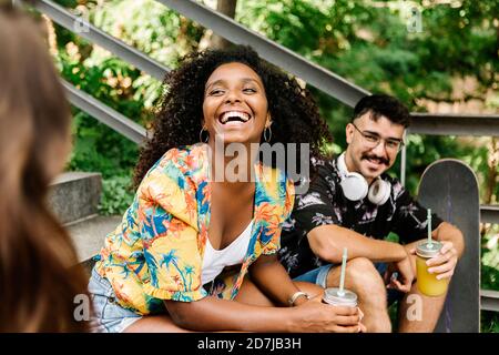 Gli amici ridono mentre bevono succo nel parco pubblico Foto Stock