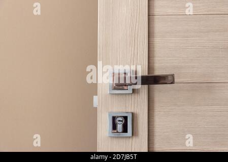 Chiudere l'elegante porta in legno con manopola e serratura vicino parete beige Foto Stock
