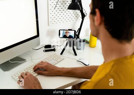 Giovane uomo che parla di videochiamata mentre lavora al computer a casa Foto Stock