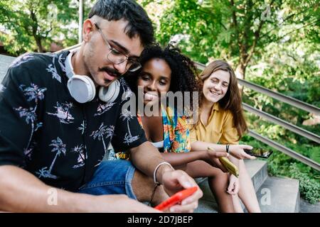 Amici che usano il telefono cellulare mentre sono seduti su una scala Foto Stock