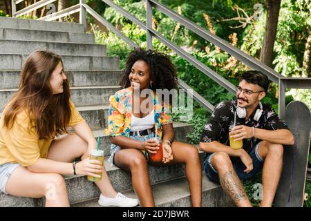 Amici seduti sui gradini mentre bevono succo nel parco pubblico Foto Stock