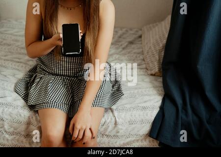 Ragazza adolescente che usa lo smartphone mentre si siede a letto camera da letto Foto Stock