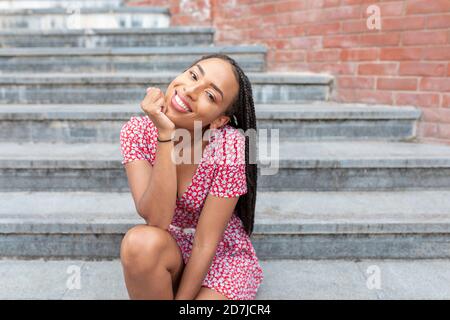 Donna sorridente con la mano sul mento seduto sulla scala dentro città Foto Stock