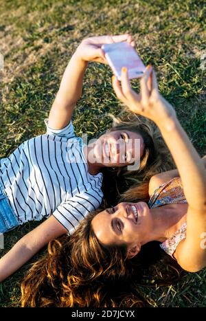 Felici le giovani donne che prendono selfie mentre si rilassano sul campo durante giorno di sole Foto Stock