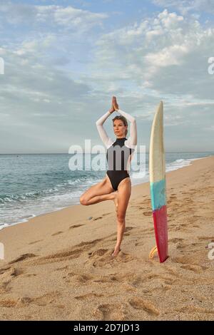 Donna che pratica yoga mentre si è in piedi dalla tavola da surf in spiaggia Foto Stock