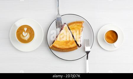 Due pezzi di torta di lamponi fatta in casa e due tazze di caffè espresso e cappuccino su un tavolo di legno bianco. Vista dall'alto. Foto Stock