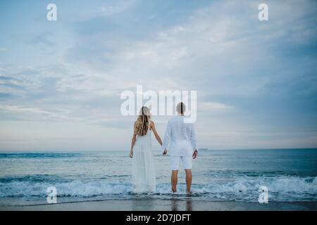 Coppia tenendo la mano mentre ammiri la vista in piedi al bordo dell'acqua sulla spiaggia Foto Stock