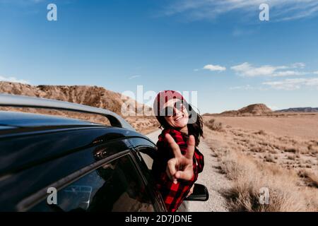 Spagna, Navarra, Ritratto di turista femminile che si appoggia fuori dalla finestra dell'auto facendo segno di pace verso la macchina fotografica Foto Stock