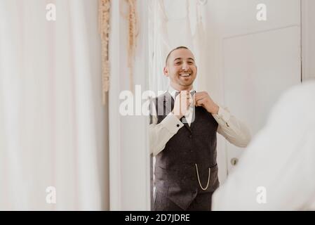 Lo sposo regola l'arco mentre si guarda nello specchio all'abito da sposa negozio Foto Stock