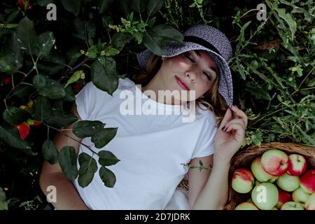 Donna mid adult che indossa cappello che dorme da mele sulla terra nel frutteto Foto Stock