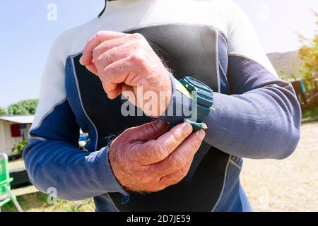 Primo piano dell'uomo anziano che indossa una muta da polso regolabile in spiaggia durante il giorno di sole Foto Stock