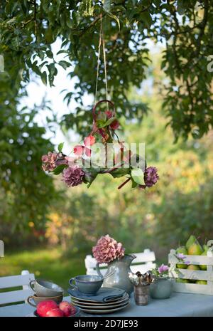 Paralume lampada fatto di foglie e idrangee in fiore appesi sopra tavolo da caffè in giardino Foto Stock