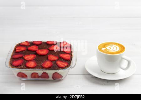 Tiramisù di fragole fatto in casa e tazza di cappuccino di caffè su tavolo di legno bianco. CopySpace. Foto Stock