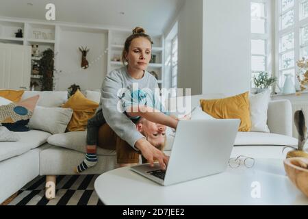 Madre che si prende cura di ragazzo mentre lavora su un computer portatile a. casa Foto Stock