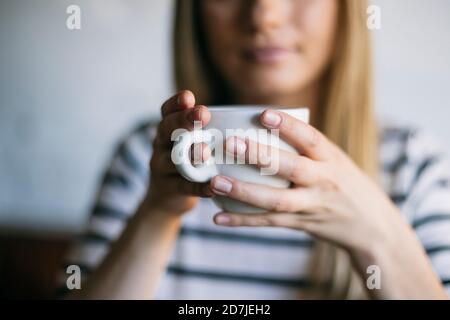 La metà della donna che tiene una tazza di caffè mentre si siede in un caffè Foto Stock