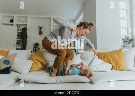 Madre gesturing mentre si sta in piedi sul divano da ragazzo a casa Foto Stock