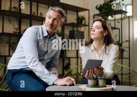 I partner che guardano fuori mentre usano il tablet digitale in ufficio Foto Stock