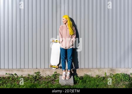 Giovane donna che guarda via con le mani in tasche in piedi contro parete metallica Foto Stock