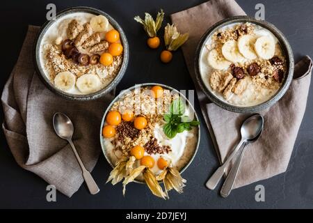 Tre ciotole di porridge con avena, semi di lino, ciliegie invernali e banane Foto Stock