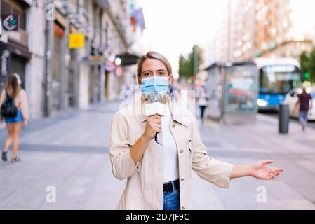 La reporter femminile indossa una maschera che parla sopra il microfono sulla strada dentro città Foto Stock