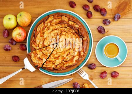 Torta fatta in casa con mele e prugne con petali di mandorle e tazza di caffè espresso su tavolo di legno. Vista dall'alto. Foto Stock