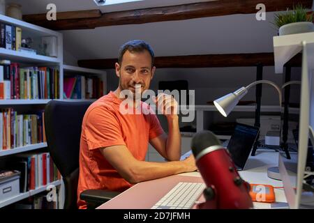 Uomo sorridente che lavora su un computer portatile mentre è seduto a casa Foto Stock