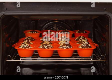 I muffin al cioccolato vengono cotti in uno stampo di silicone rosso all'interno di un forno domestico. Messa a fuoco superficiale. Foto Stock