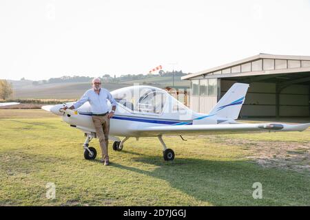 Uomo anziano con mano sull'anca in piedi contro l'aereo a. campo aereo Foto Stock