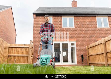 Uomo medio adulto che utilizza il rasaerba per la falciatura in cortile Foto Stock