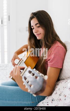 Giovane donna che suona la chitarra a casa in camera da letto Foto Stock