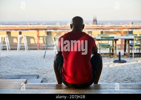 Uomo maturo in t-shirt rossa seduto sui gradini sul tetto durante il tramonto Foto Stock