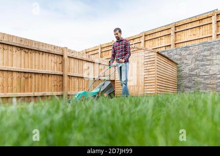 Uomo che usa il tosaerba mentre cammina in cortile Foto Stock
