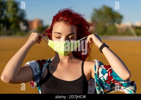 Giovane donna che indossa una maschera protettiva mentre si sta in piedi all'aperto giorno di sole Foto Stock