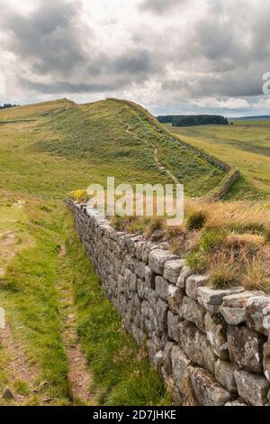 Regno Unito, Inghilterra, Hexham, nuvole su verdi colline erbose e parte del Muro di Adriano Foto Stock