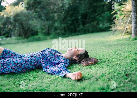 Giovane donna che si rilassa su terra erbosa contro le piante nel parco Foto Stock