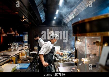 Gli chef indossano una maschera protettiva per la preparazione del piatto nella cucina del ristorante Foto Stock