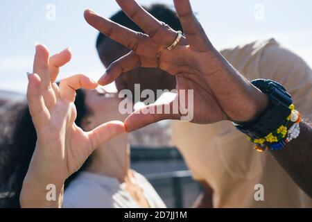 Bacia in coppia mentre si fa il cuore con le dita in piedi in città Foto Stock