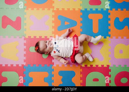 Cute baby girl mentendo su colorful puzzle alfabetico playmat a. casa Foto Stock