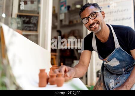 Sorridente vasaio maschio con miniature sul tavolo lavorando in officina Foto Stock