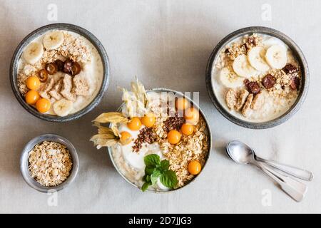 Tre ciotole di porridge con avena, semi di lino, ciliegie invernali e banane Foto Stock