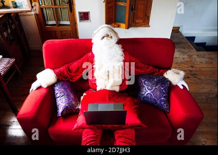 Uomo che indossa il costume di Babbo Natale con computer portatile che si rilassa sul divano a casa Foto Stock