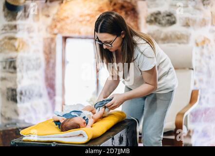 Madre che cambia pannolino di bambino mentre si siede a casa Foto Stock