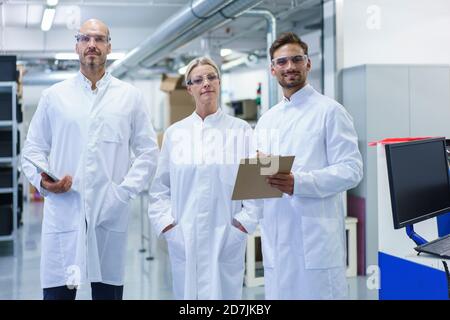 Scienziati di sesso maschile e femminile sicuri in piedi in camice bianco da laboratorio presso il laboratorio illuminato Foto Stock