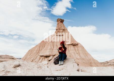 Spagna, Navarra, turista femminile utilizzando smartphone di fronte alla formazione di pietra arenaria in Bardenas Reales Foto Stock