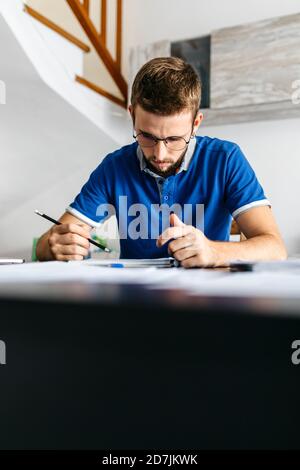 Bell'uomo giovane che studia mentre si siede a tavola Foto Stock