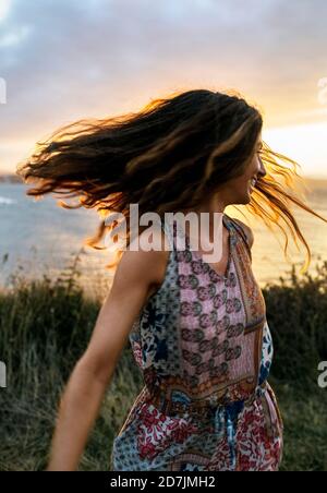 Giovane donna allegra che lancia i capelli contro il cielo durante il tramonto Foto Stock